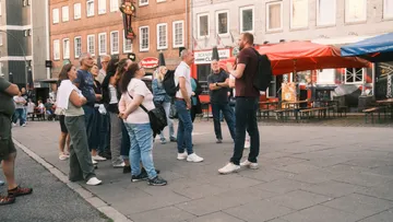 Tour group listening to guide in city square.