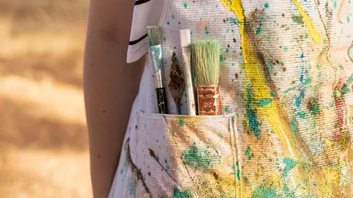Paintbrushes in colorful splattered apron pocket.