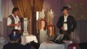 Two men present copper stills on a stage.