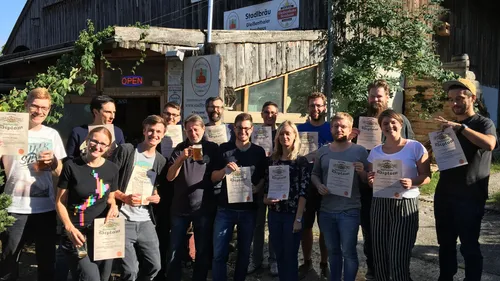 Gruppe posiert mit Urkunden vor einer Brauerei.