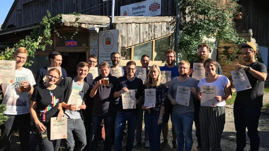 Gruppe posiert mit Urkunden vor einer Brauerei.
