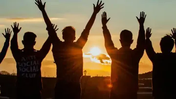 Vier Personen heben Arme bei Sonnenuntergang.