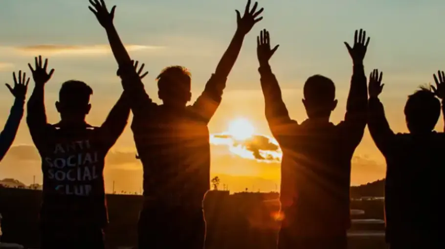 Vier Personen heben Arme bei Sonnenuntergang.