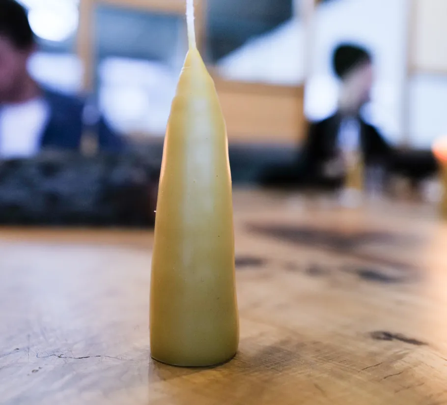 Gelbe Kerze auf Holztisch, unscharfer Hintergrund.