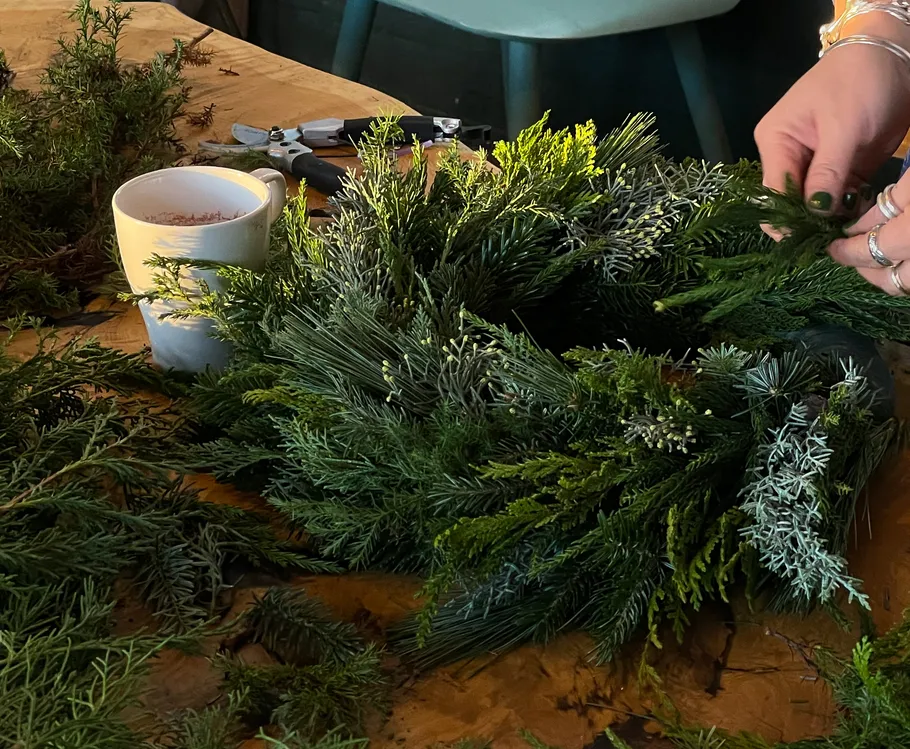 Hands crafting a wreath on wooden table.
