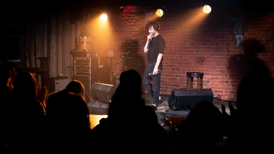 Komiker tritt auf Bühne in dunklem Comedy-Club auf.