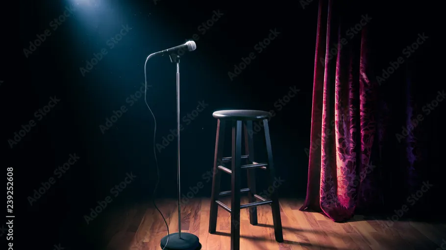 Microphone and stool on stage with spotlight.