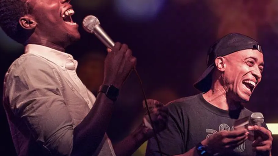 Two men laughing, holding microphones on stage.