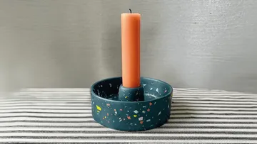 Orange Kerze auf Terrazzo-Halter, gestreifte Oberfläche.