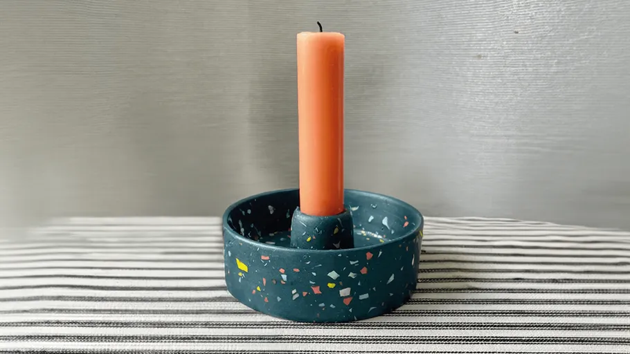Orange Kerze auf Terrazzo-Halter, gestreifte Oberfläche.