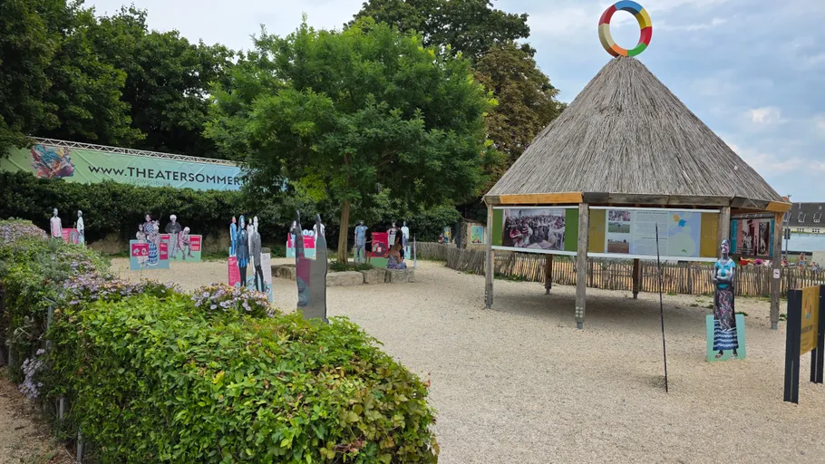 Kunstinstallation im Freien mit Holzfiguren und Hütte.