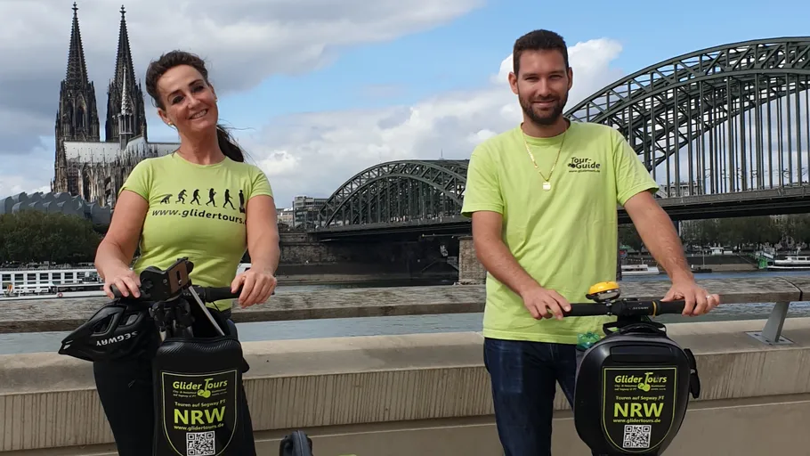 Two people on scooters near Cologne Cathedral.