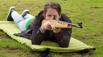Person aiming rifle while lying on grass.