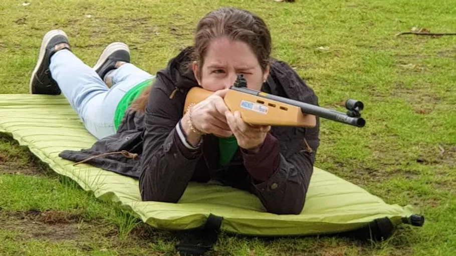 Person aiming rifle while lying on grass.