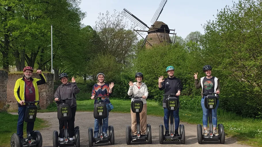 Six people on Segways near a windmill.