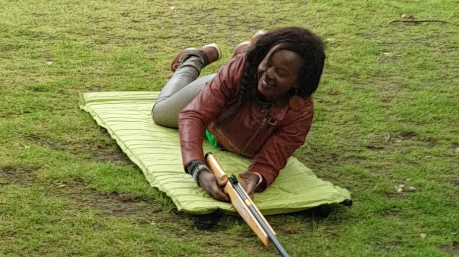 Person aiming rifle while lying on grass.