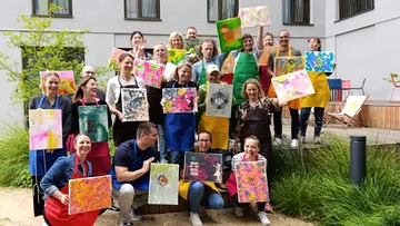 Group holding colorful paintings outdoors.