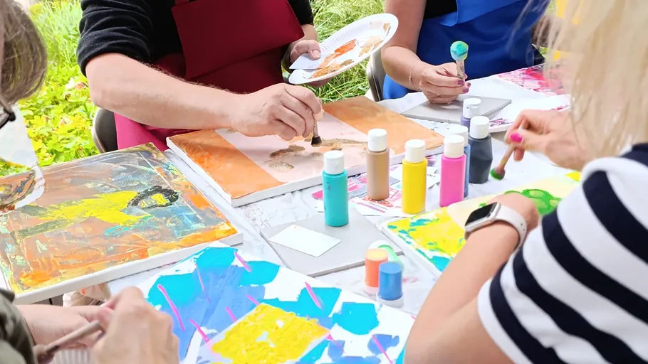 People painting with brushes at outdoor table.