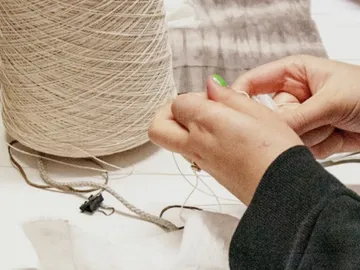 Hands hold thread, sew next to a ball of wool.