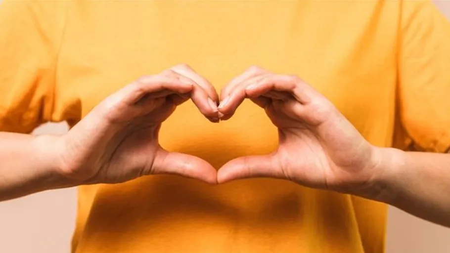 Hands forming heart shape, yellow shirt.