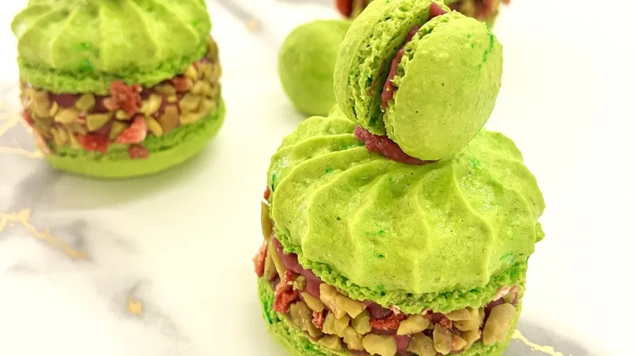 Green macarons with nut filling on marble surface.