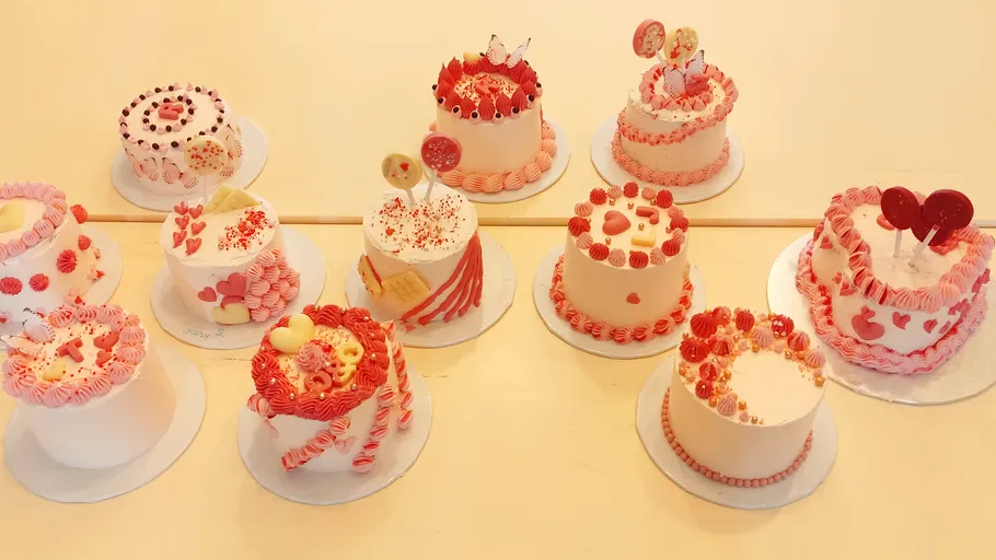Nine decorated cakes with pink icing displayed.