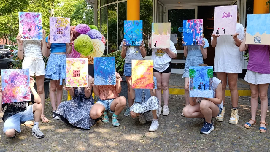 Personen halten bunte Gemälde vor einem Gebäude.
