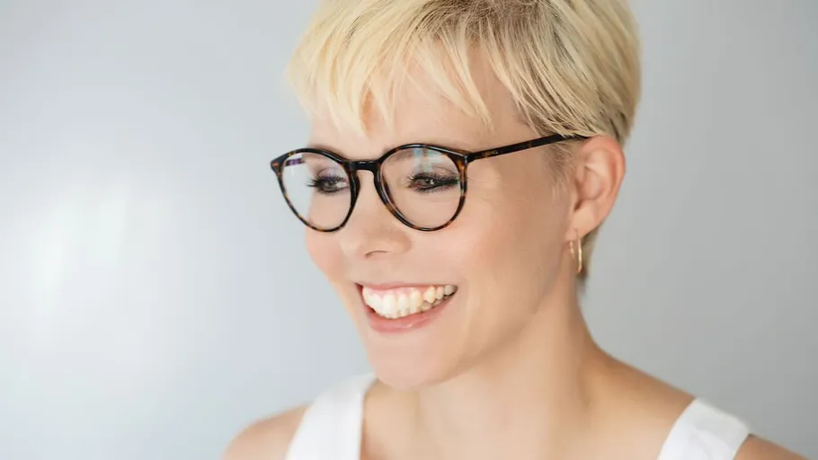 Lächelnde Person mit Brille, heller Hintergrund.