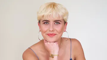 Person with short blond hair smiling indoors.
