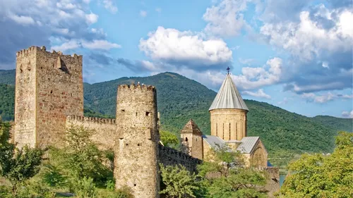 Steinburg und Kirche in grüner Landschaft.