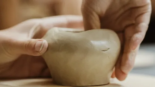Hands shaping clay pottery indoors.