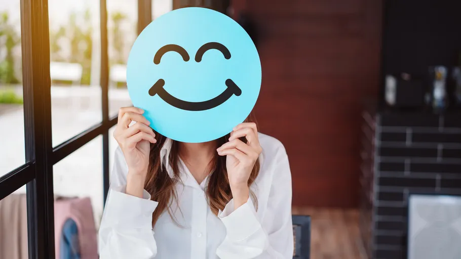 Person holding blue smiley face sign indoors.