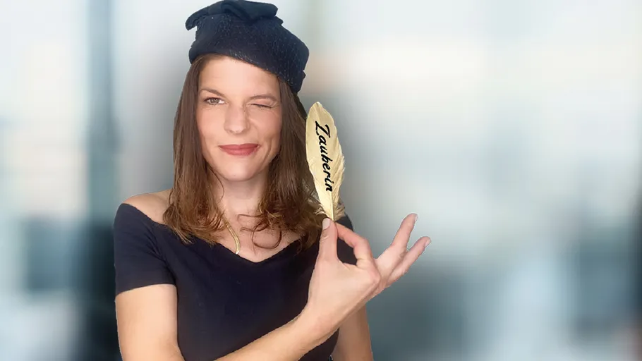 Frau zwinkert, hält Feder, drinnen.