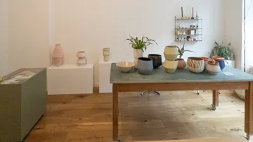 Keramiktöpfe auf Holztisch in Innenraum ausgestellt.