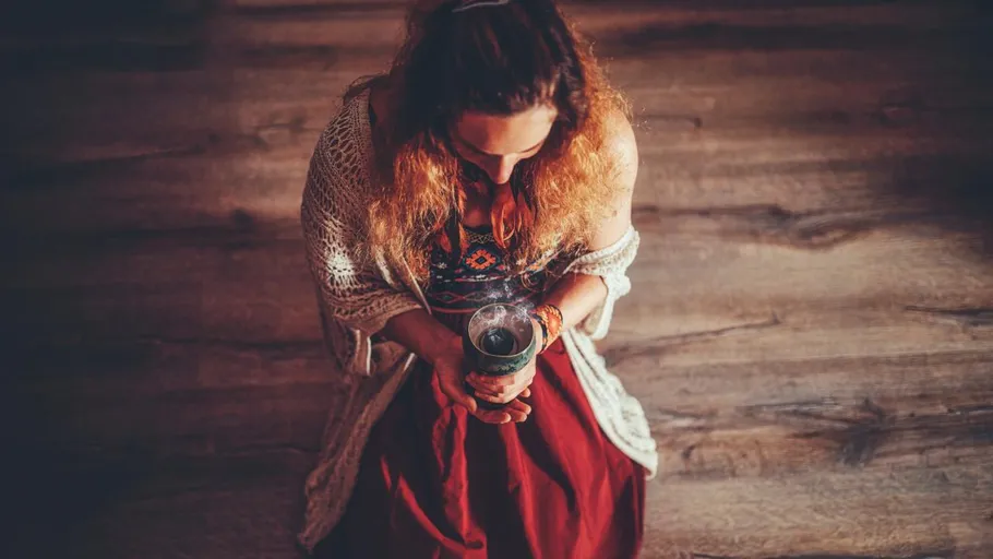 Person holding cup sitting on wooden floor.