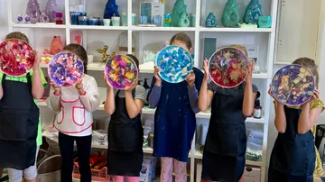 Children holding decorated plates in art room.