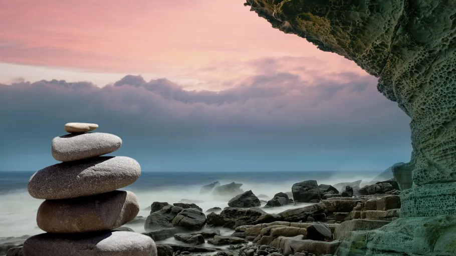 Stacked stones by a rocky shoreline at sunset.