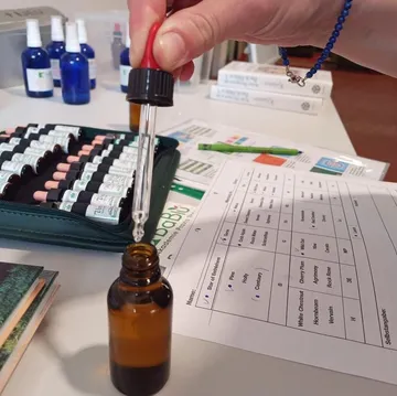 Hand pipetting liquid into a bottle beside documents.