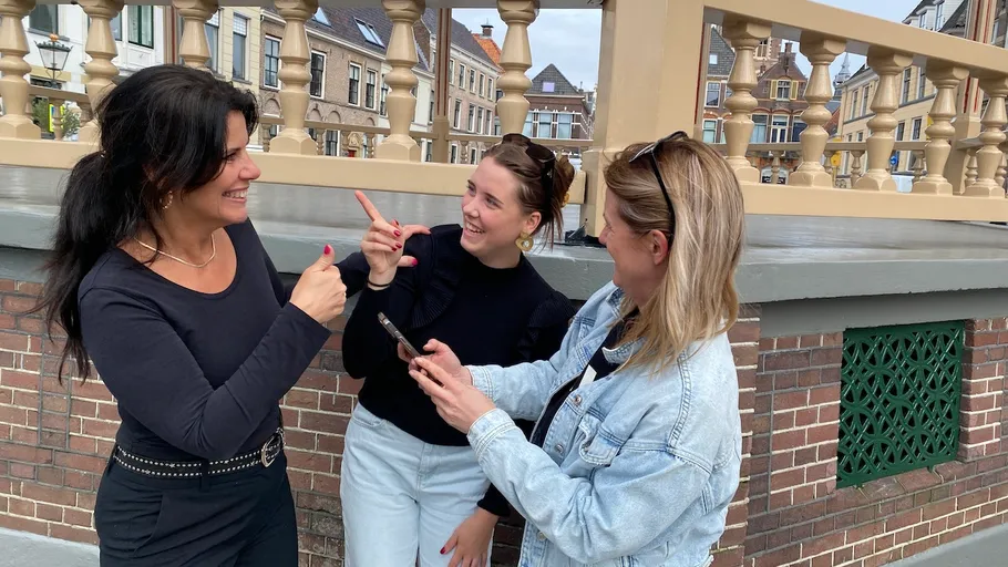 Drei Frauen lächeln und sprechen draußen.