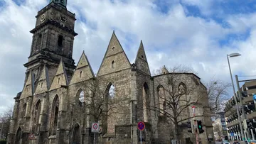 Gothic church ruins with tower, cloudy sky.