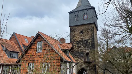 Steinturm neben roten Dächern, bewölkter Himmel.