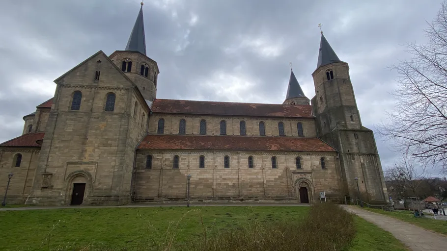Large stone church with three spires, cloudy sky.