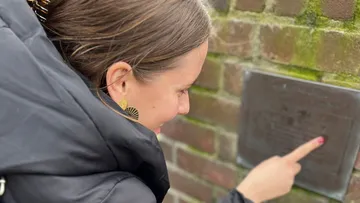 Woman pointing at a plaque on a brick wall.