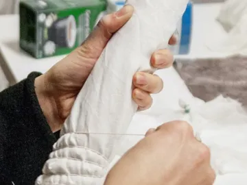 One hand holds a white fabric while sewing.