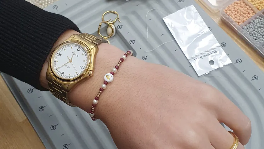 Hand mit Uhr und Armband auf Bastelunterlage.