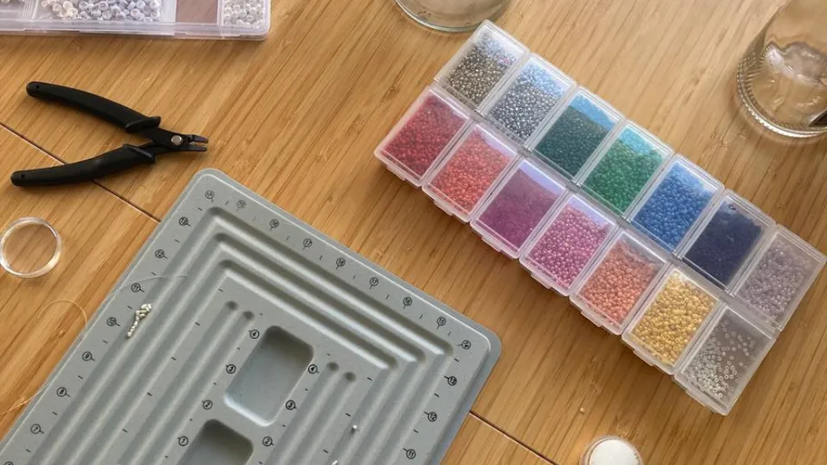 Perlenwerkzeuge und bunte Perlen auf Tisch.