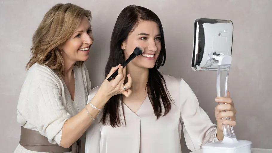 Two women applying makeup, smiling at mirror.