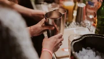 Hands shaking cocktail mixer in a bar.