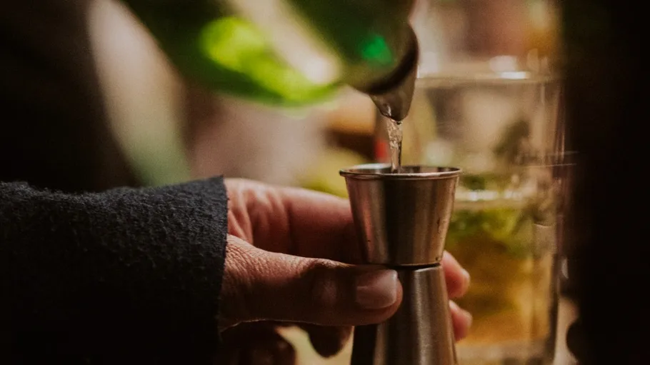 Hand gießt Flüssigkeit in einen Jigger.