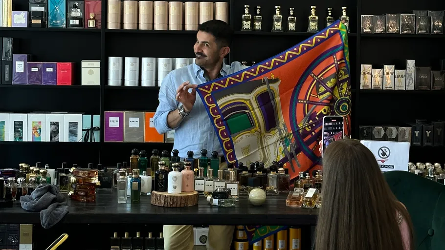 Man displays colorful scarf in perfumery shop.